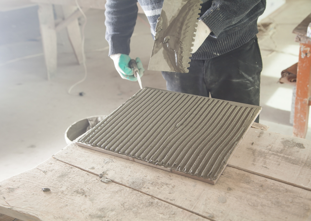 Worker putting tiles adhesive to the floor.